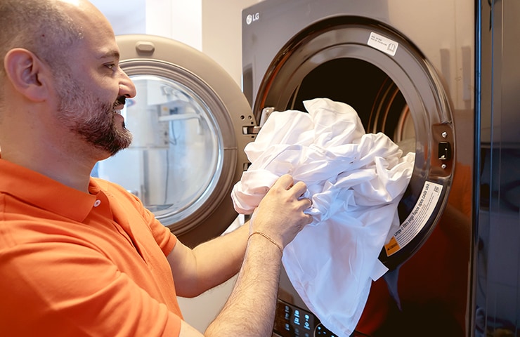 Padre poniendo la ropa en LG WashTower, en la unidad superior que es una secadora con una sonrisa en su cara.